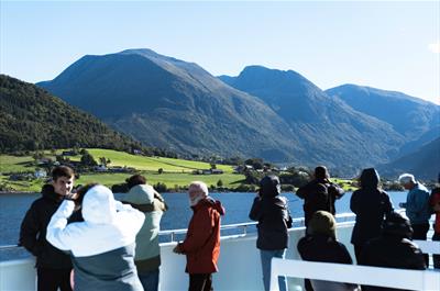 Turistar på dekk på Hardangerfjordekspressen som nyt utsikta av fjord og fjell i Hardanger.