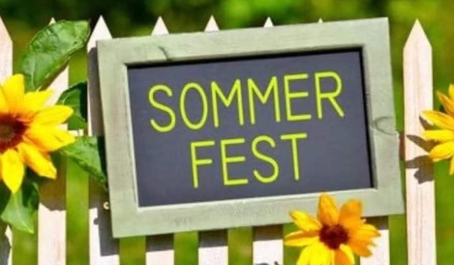 «SOMMERFEST» står det på et skilt som henger på et gjerde dekorert med solsikker