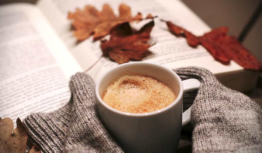 Åpen bok med gul-røde eikeblader på og en kopp kaffe