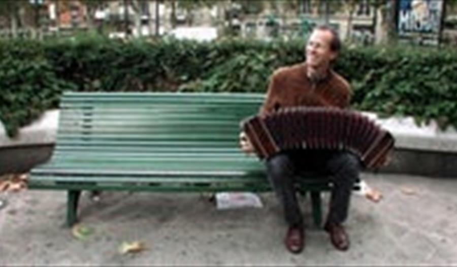 En man sitter på benken and spiller trekkspill