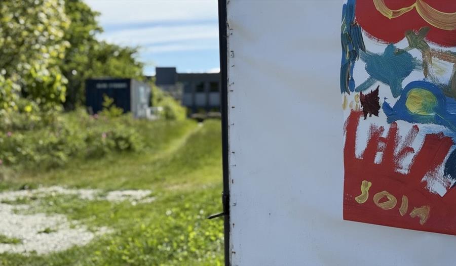 Utsikt fra den åpne døren: grå bygning og en del av plakat  med SOLA skrevet på