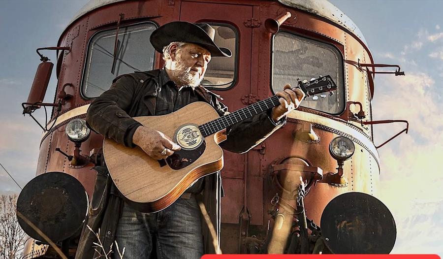 Arly Karlsen med gitar foran en gamel tog