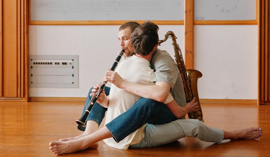 Utsnitt fra forestillingen 'Koreografi for to Musikere' - to menn med musikkinstrumenter som sitter veldig tett inntil hverandre