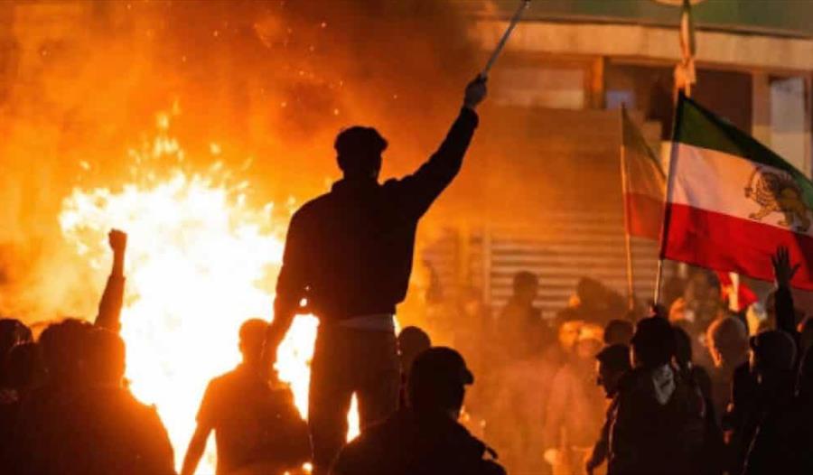 Personer med iranske flagg deltar i møtet med en brann i bakgrunnen.