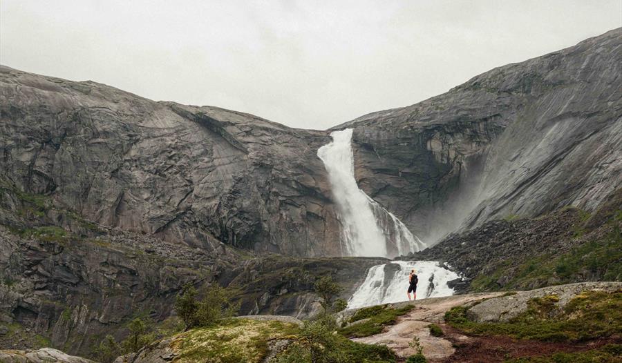 To turgåarar står framfor den mektige Søtefossen i Husedalen, omringa av dramatiske fjell og fossande vatn.