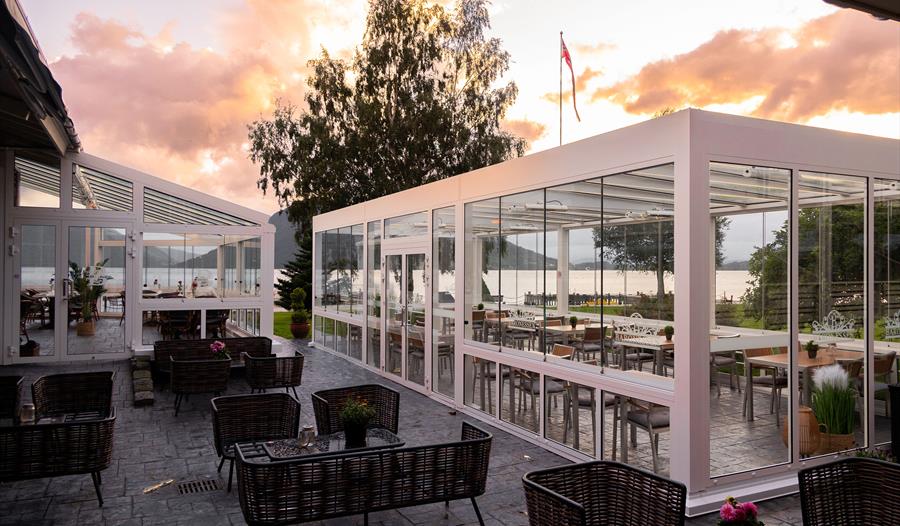 Uteservering og glasveranda ved Restaurant Baronen i Rosendal med utsikt mot Hardangerfjorden i varmt kveldsljos.