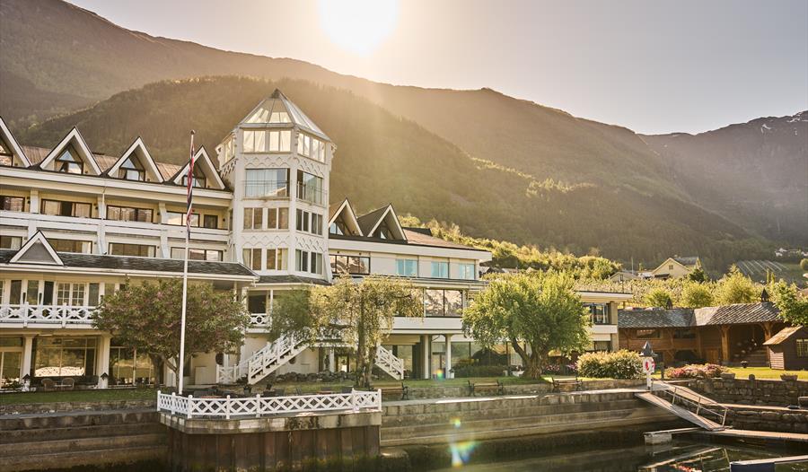 Hotel Ullensvang med hage og fjordutsikt i gyllen kveldssol – ein klassikar i Hardanger.