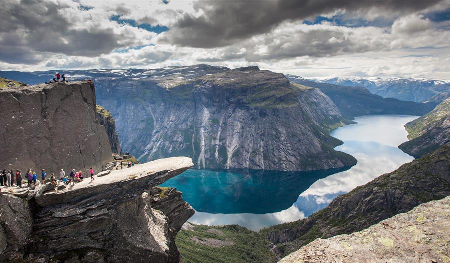 Spektakulær utsikt frå Trolltunga, eit av Noregs mest ikoniske fjellformasjonar, med blått vatn og dramatiske fjell i bakgrunnen.