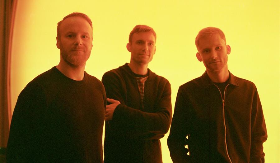 Erlend Apneseth Trio foran en gul vegg
