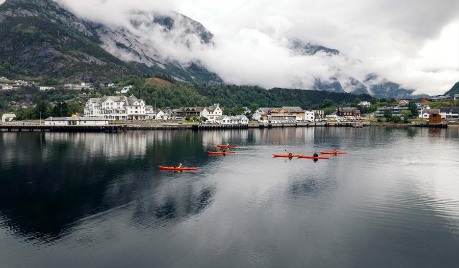 Flere røde kajakker på fjorden, med Eidfjord sentrum i bakgrunnen.