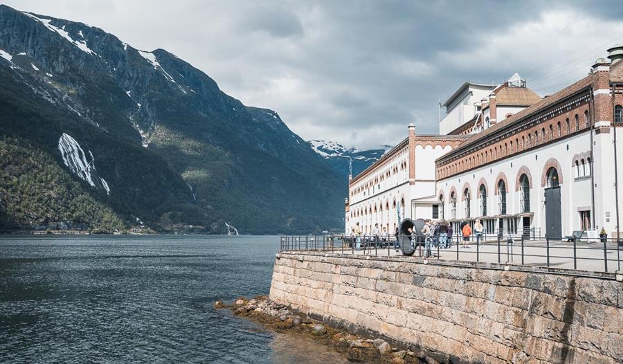 Bygningar frå Kraftmuseet i Hardanger med utsikt over fjorden, omgitt av vakre fjell og norsk natur.
