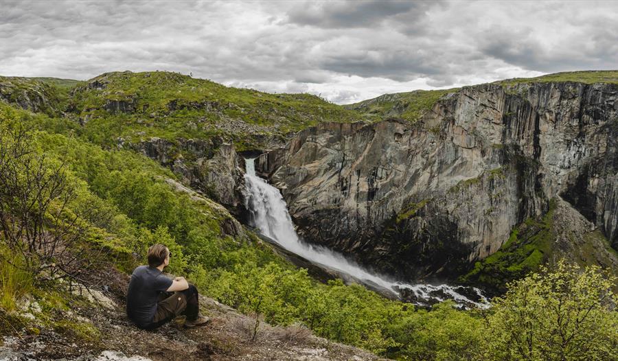 En mann sitter på bakken og ser på Valurfossen nedenfor.