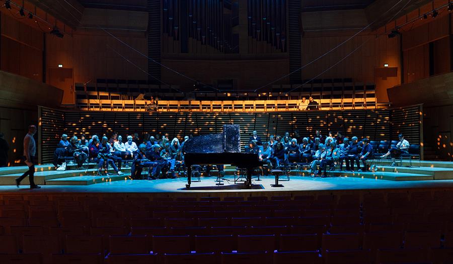 En artist som spiller på en piano i en stor konsertsal med publikum tett rundt seg.