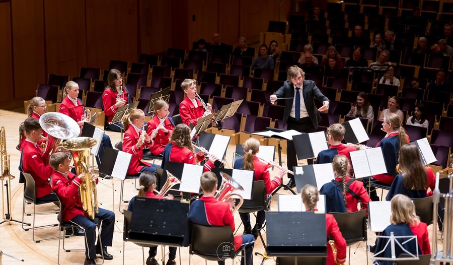 Et skoleorkester som opptrer på scenen med en dirigent som leder dem.