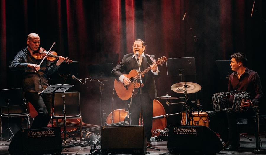 Mollo trio som spiller ulike instrumenter på en scene