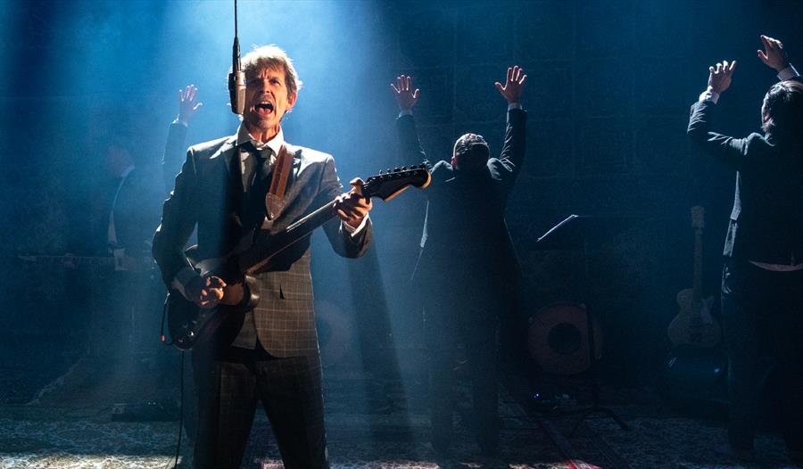 Utdrag fra fremføringen, en mann står på scenen og synger i mens han spiller gitar