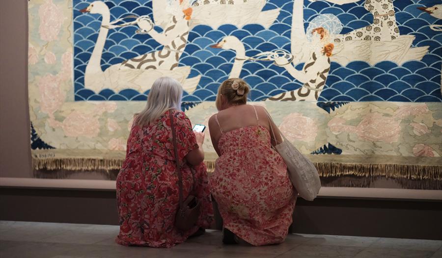 To kvinner i blomstrete kjoler kikker på verket "Sørover" av Frida Hansen
