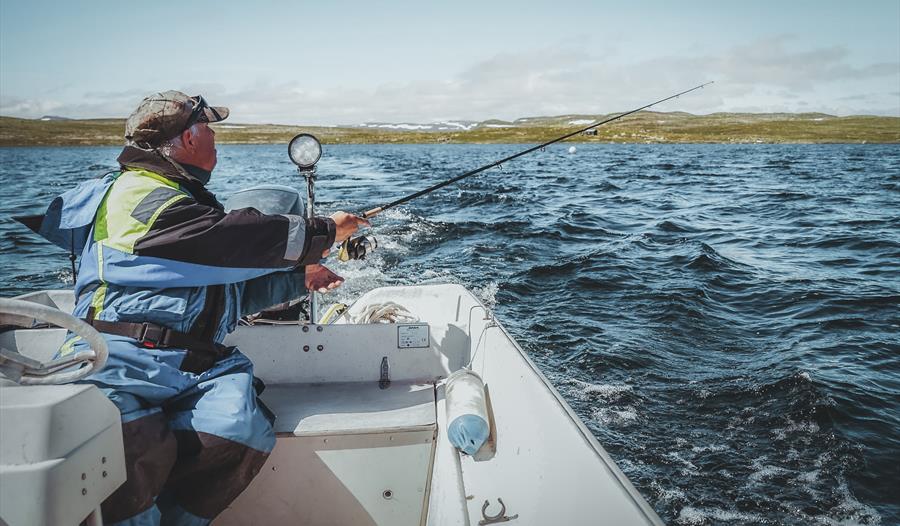 En mann fisker fra båt ved Halnefjorden på Hardangervidda.