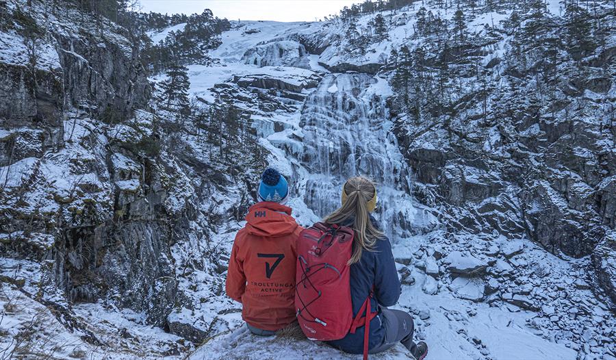 To turister sitter og nyter utsikten over et isdekt fossefall i Husedalen.