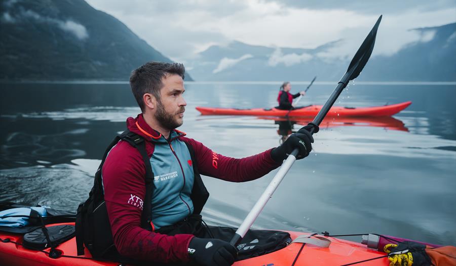 Et par padler kajakk i to røde kajakker på fjorden.