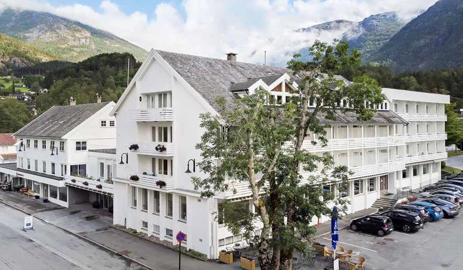 Fasaden til Kinsarvik Fjordhotel med idyllisk utsikt mot Hardangerfjorden, omgitt av vakker natur og fjellandskap.