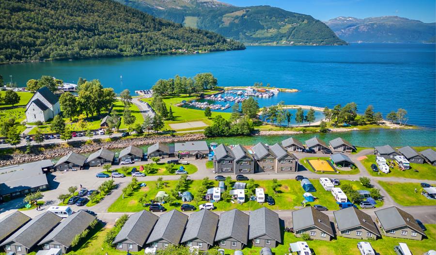 Luftfoto av Mikkelparken Ferietun i Kinsarvik, omgitt av Hardangerfjorden og majestetiske fjell. Perfekt feriestad for heile familien.