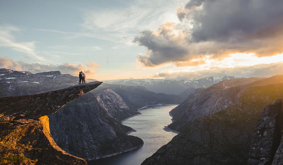 Et kjærestepar står på Trolltunga og ser utover Ringeldasvatnet.