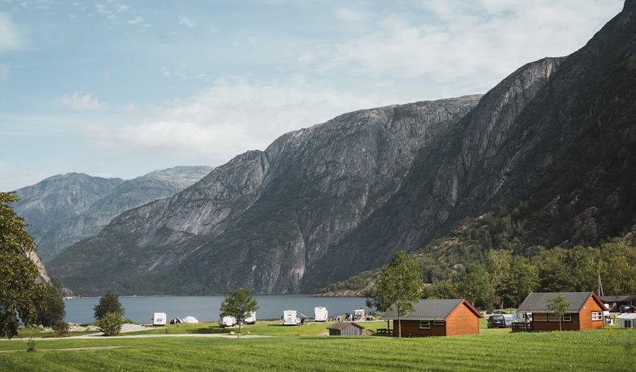 Sæbø camping sett fra hovedveien, med vann og fjell i bakgrunnen.