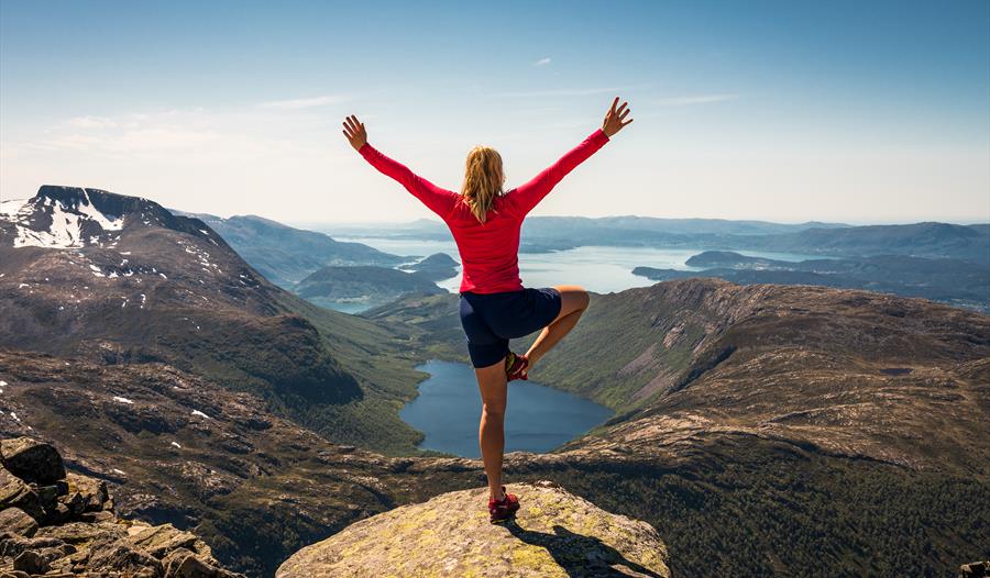 Kvinne står og poserer og ser utover panoramautsikt mot fjord og fjell.
