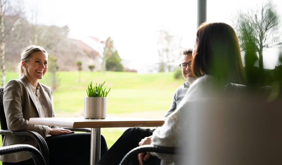 Tre personer sitter rundt et bord og snakker på Bryne Kro & Hotell