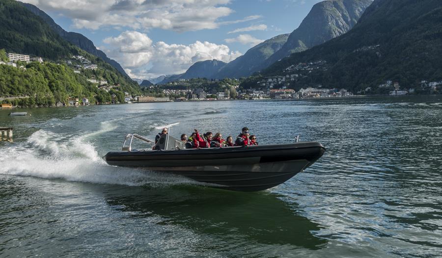 RIB-båt susar over Hardangerfjorden med spektakulære fjell i bakgrunnen.