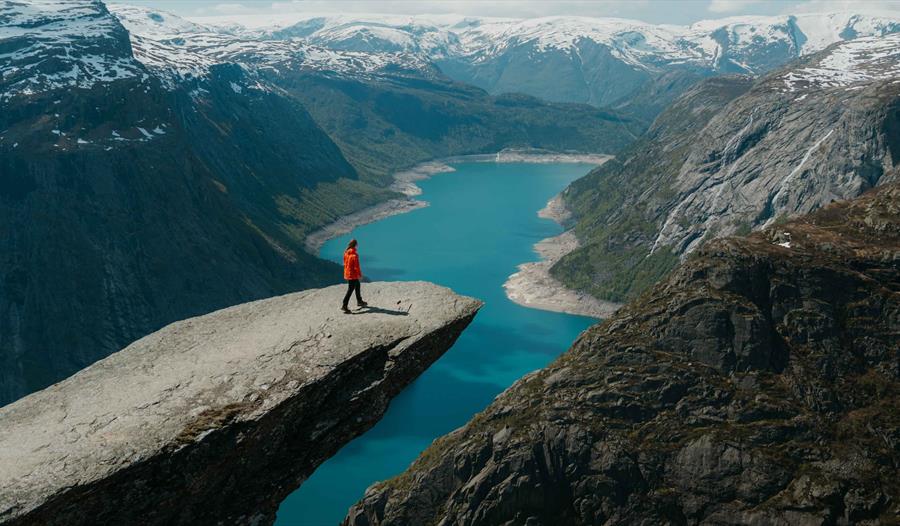 Ein turgåar står ytterst på Trolltunga og ser utover Ringedalsvatnet og dei dramatiske fjella i Hardanger.