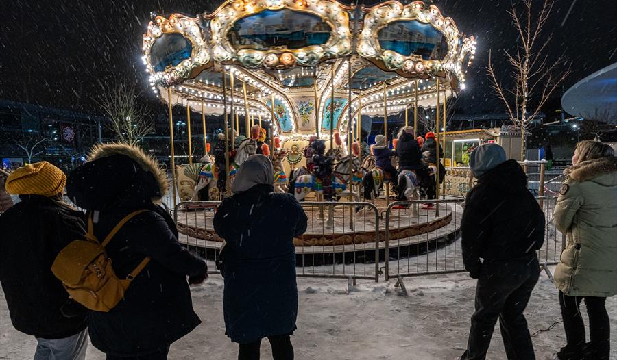 Barn på en karuselltur under et vintermarked, folk står spredt rundt karusellen og ser på barna sine.