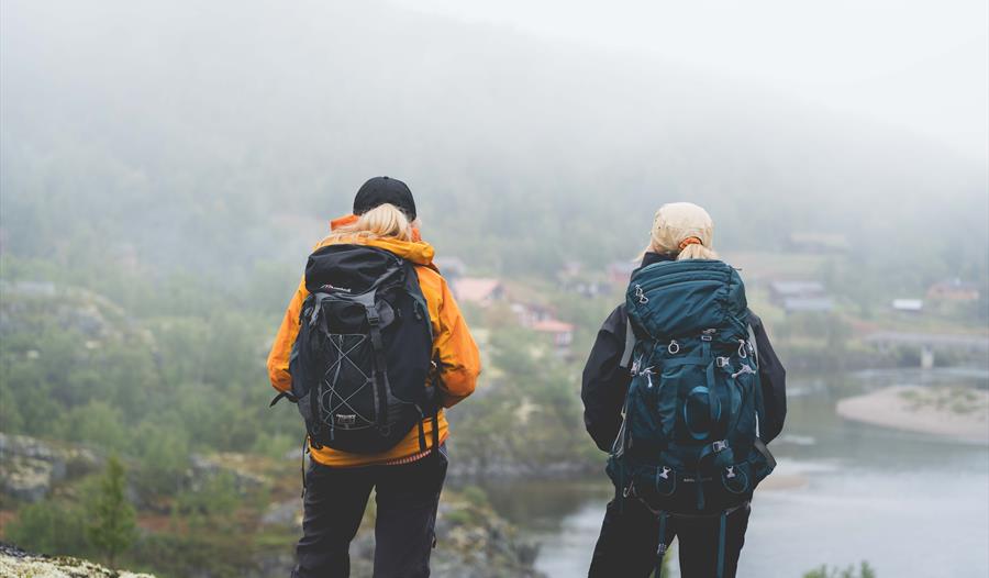 To turgåere stirrer mot Vivelid Fjellstova fra den andre siden av elva.