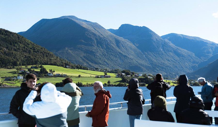 Turistar på dekk på Hardangerfjordekspressen som nyt utsikta av fjord og fjell i Hardanger.