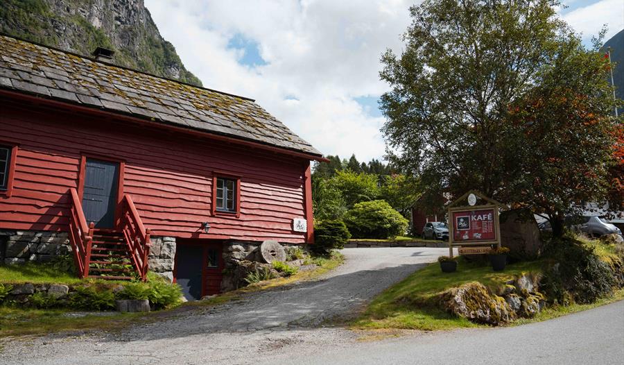 Den raude, tradisjonelle låvebygningen til Olaløo i Bondhus, Hardanger, omgitt av frodig natur og fjell.