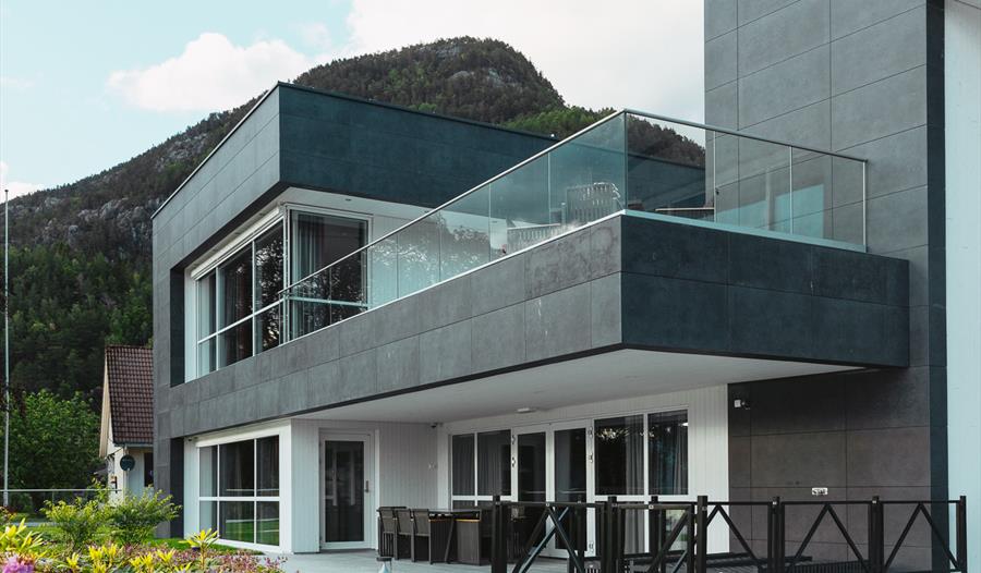 Moderne fasade av Hardanger House med romsleg balkong og fjordutsikt.