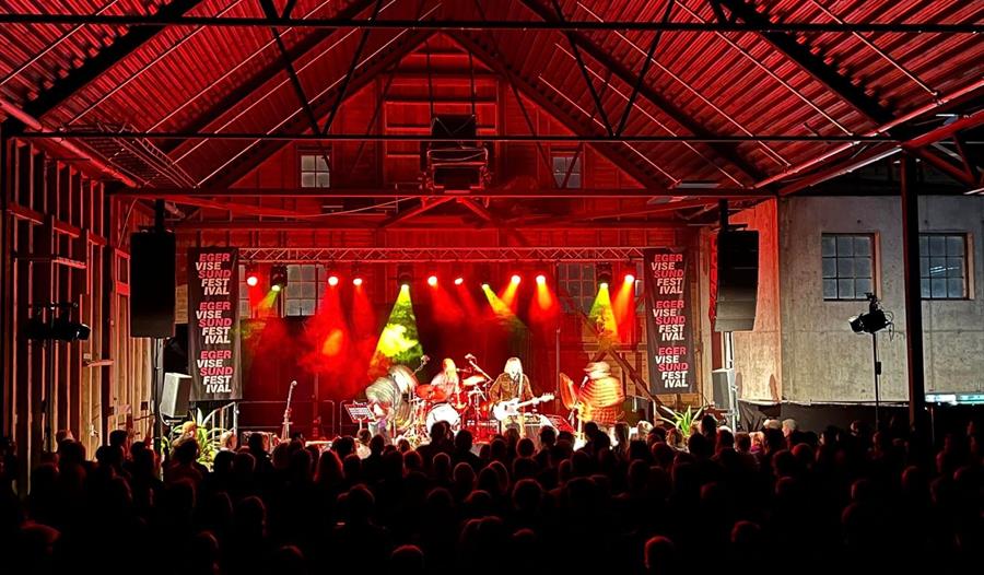 Band playing on stage with audience. Red stage lights.