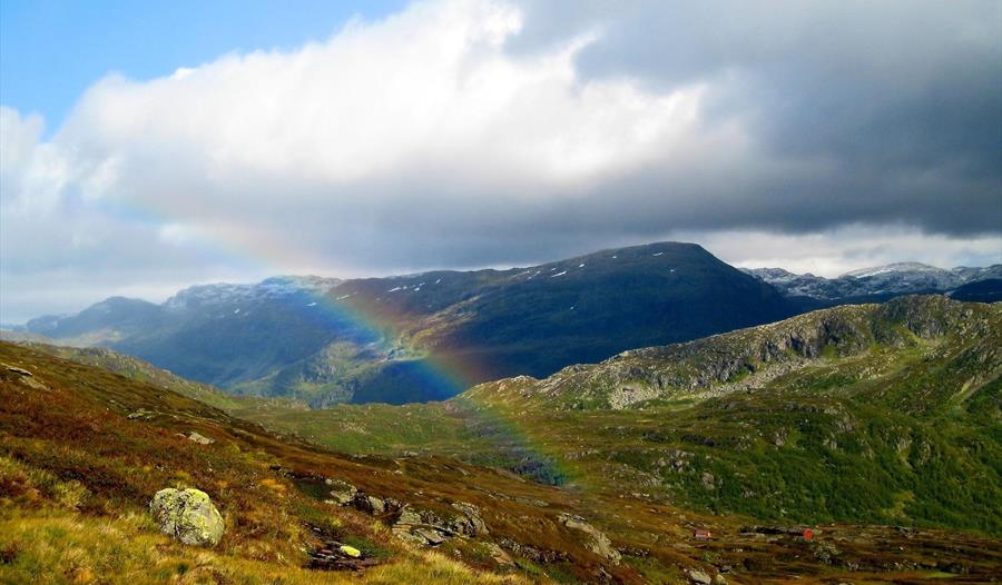 Utsikt over fleire fjell med regnboge midt i bildet