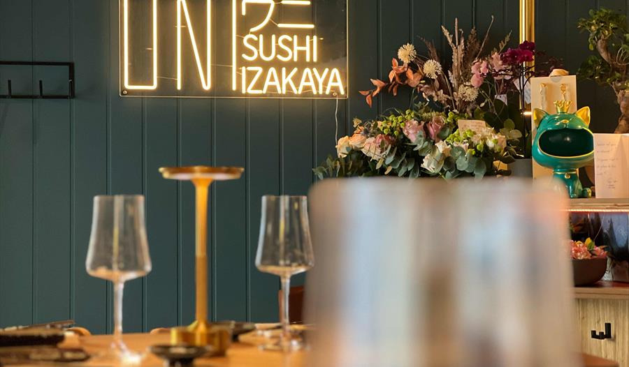 Interiør av UNI Sushi & Izakaya med neon-skilt og blomsterdekorasjoner.