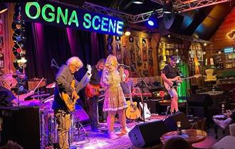 En mann spiller gitar og en kvinne synger på scenen på Ogna Scene