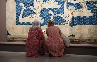 To kvinner i blomstrete kjoler kikker på verket "Sørover" av Frida Hansen