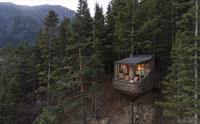 Ei moderne tretopphytte frå Woodnest i Odda, Hardanger, omgitt av tett skog og mektige fjell.