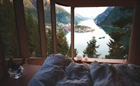 Morgonutsikt frå senga i Woodnest tretopphytte – fjorden, fjella og småbyen Odda i soloppgangen.