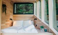 Ei seng med mjuke tekstilar og store vindauge som slepp inn naturlyset i Woodnest tretopphytte.