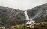 To turgåarar står framfor den mektige Søtefossen i Husedalen, omringa av dramatiske fjell og fossande vatn.