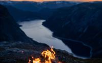 Bålpanne med åpen ild på en fjelltopp ved solnedgang med utsikt over en fjord.