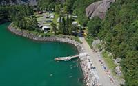 Badeplass ved Trolltunga Camping med brygge, badande gjester og campingplassen langs vatnet.