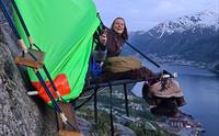 Ei kvinne smiler frå ein portaledge med spektakulær utsikt over fjorden og fjella i Hardanger. Eit adrenalinfylt overnattingseventyr.