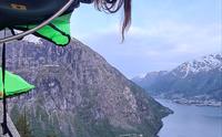 Ei kvinne smilar og stikk hovudet ut frå ein portaledge, med fjorden langt under ho i Hardanger. Eit eventyrleg overnattingsalternativ.